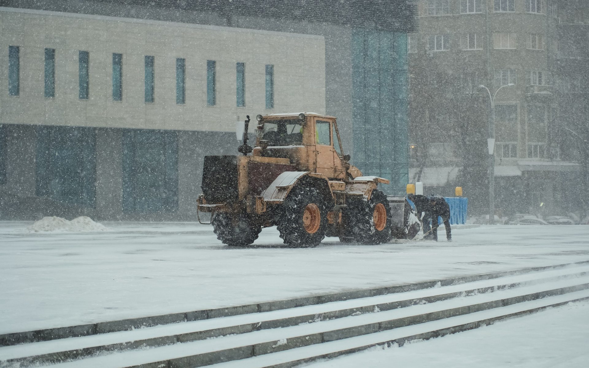 A snowplow and worker clearing snow in Kharkiv, Ukraine, on a snowy winter day.