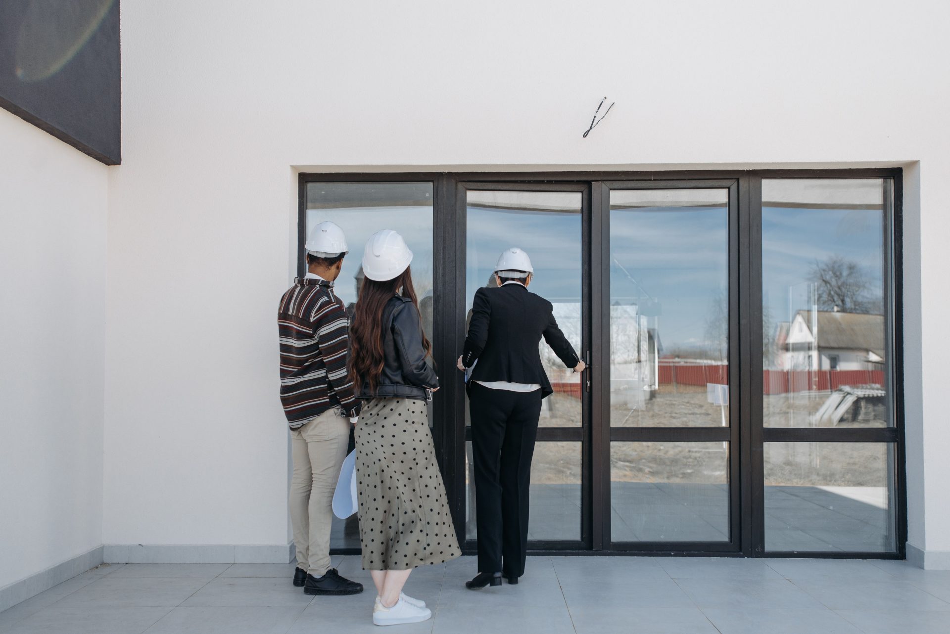 Immobilienmakler mit Helmen zeigen Kunden durch Glastüren ein neues Haus.